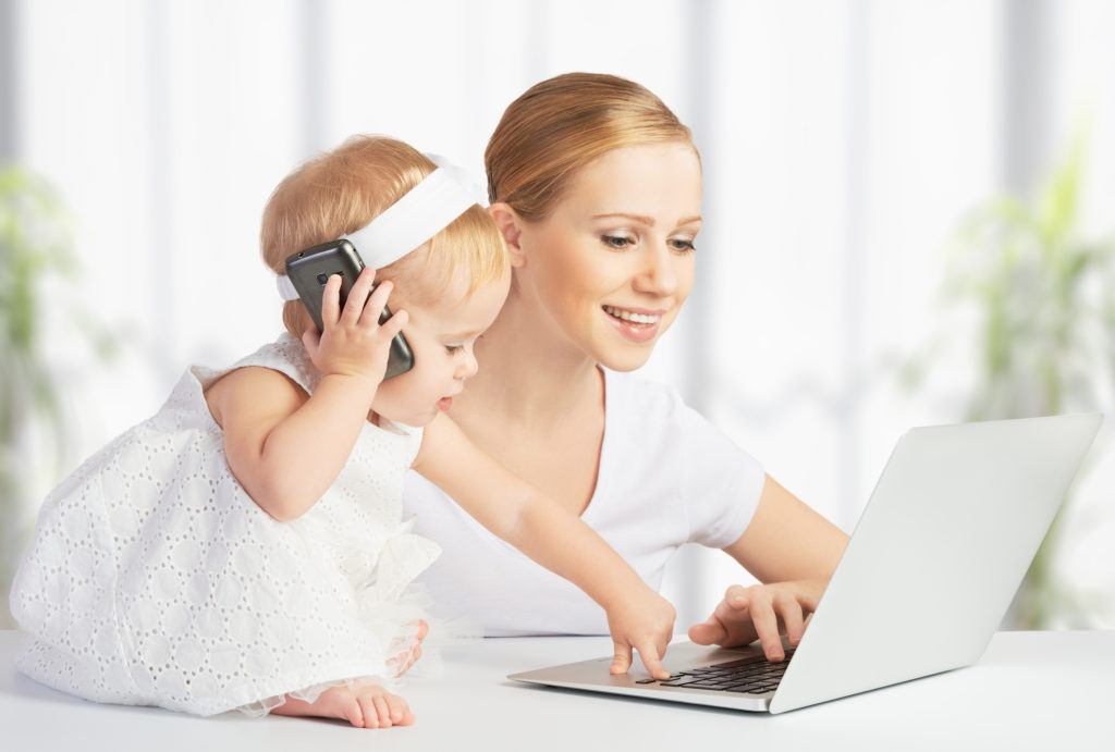 young mother with baby daughter works on the Internet with a computer and phone